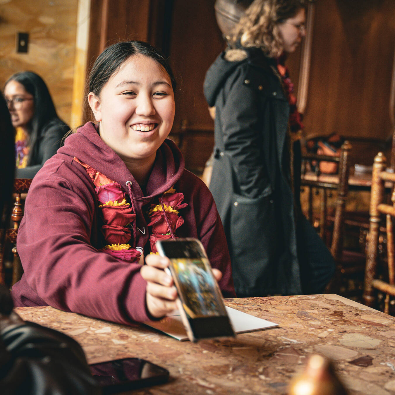 A girl smiling and showing a photo on her phone to another student